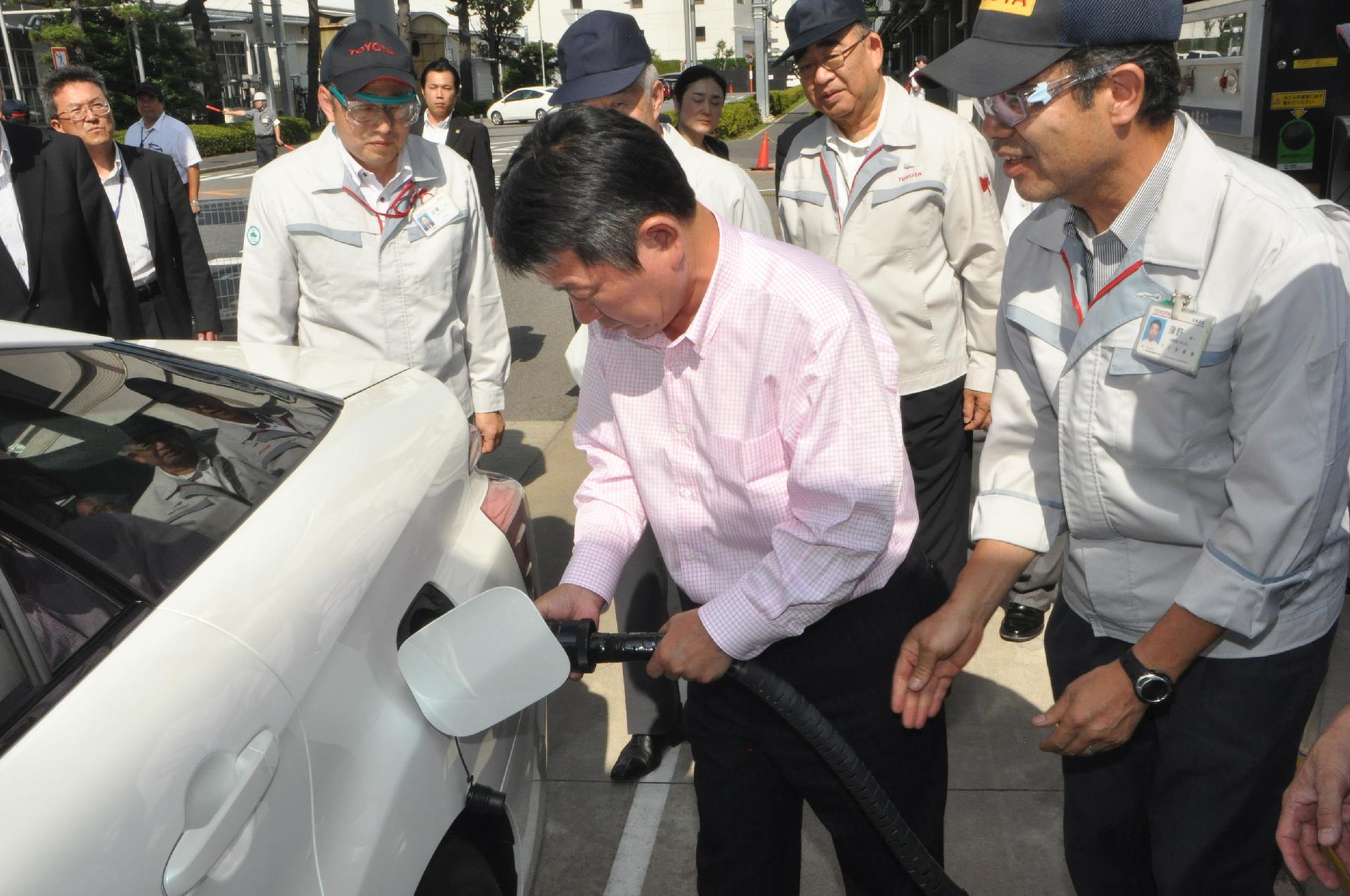 Toshimitsu Motegi, Japanese Minister of Economy, Trade and Industry (center), refuels Toyota's fuel cell sedan