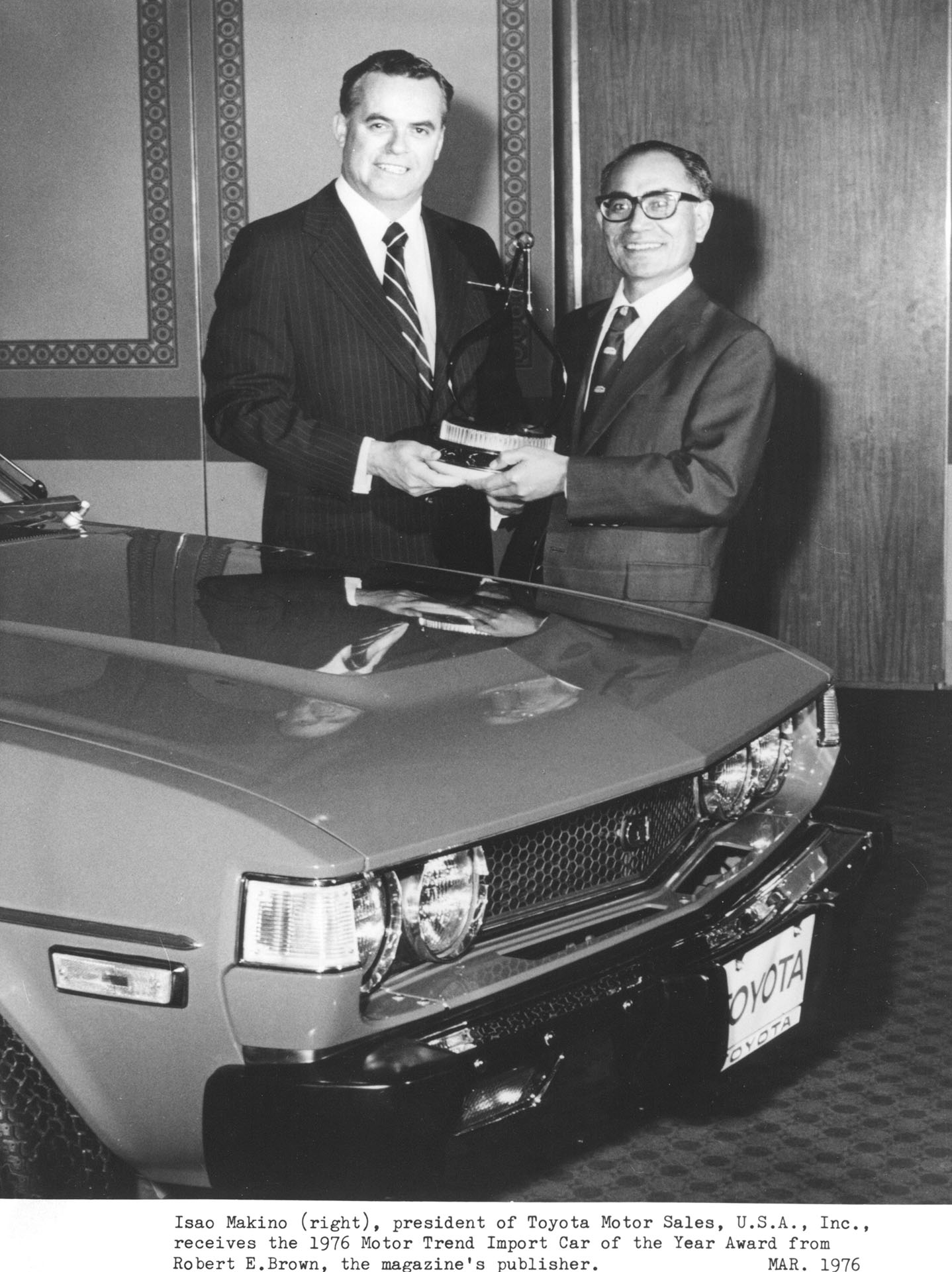 Isao Makino (right), president of Toyota Motor Sales, U.S.A., Inc., receives the 1976 Motor Trend Import Car of the Year Award from Robert E. Brown, the magazine's publisher.